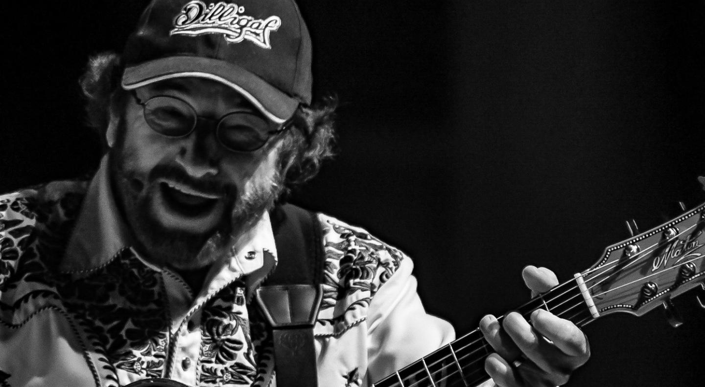 A close up black and white shot of Kevin Bloody Wilson laughing as he plays guitar