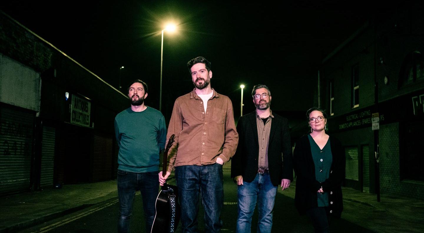 Kris Drever and his band walk along a dark street lit by streelights