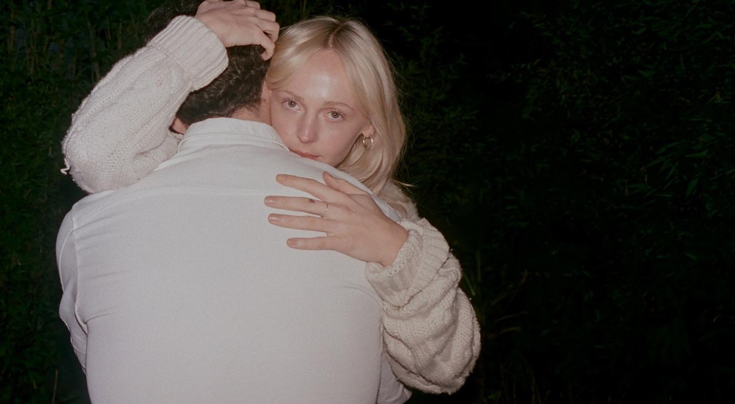 Laura Marling embraces a man with one hand cradling his head. She looks out at the camera over his shoulder
