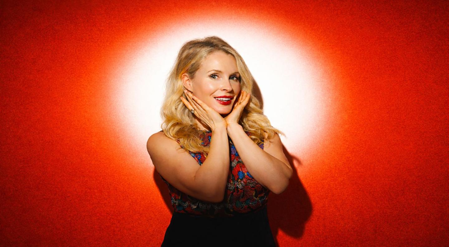 A photograph of Lucy Beaumont posing in front of a red background