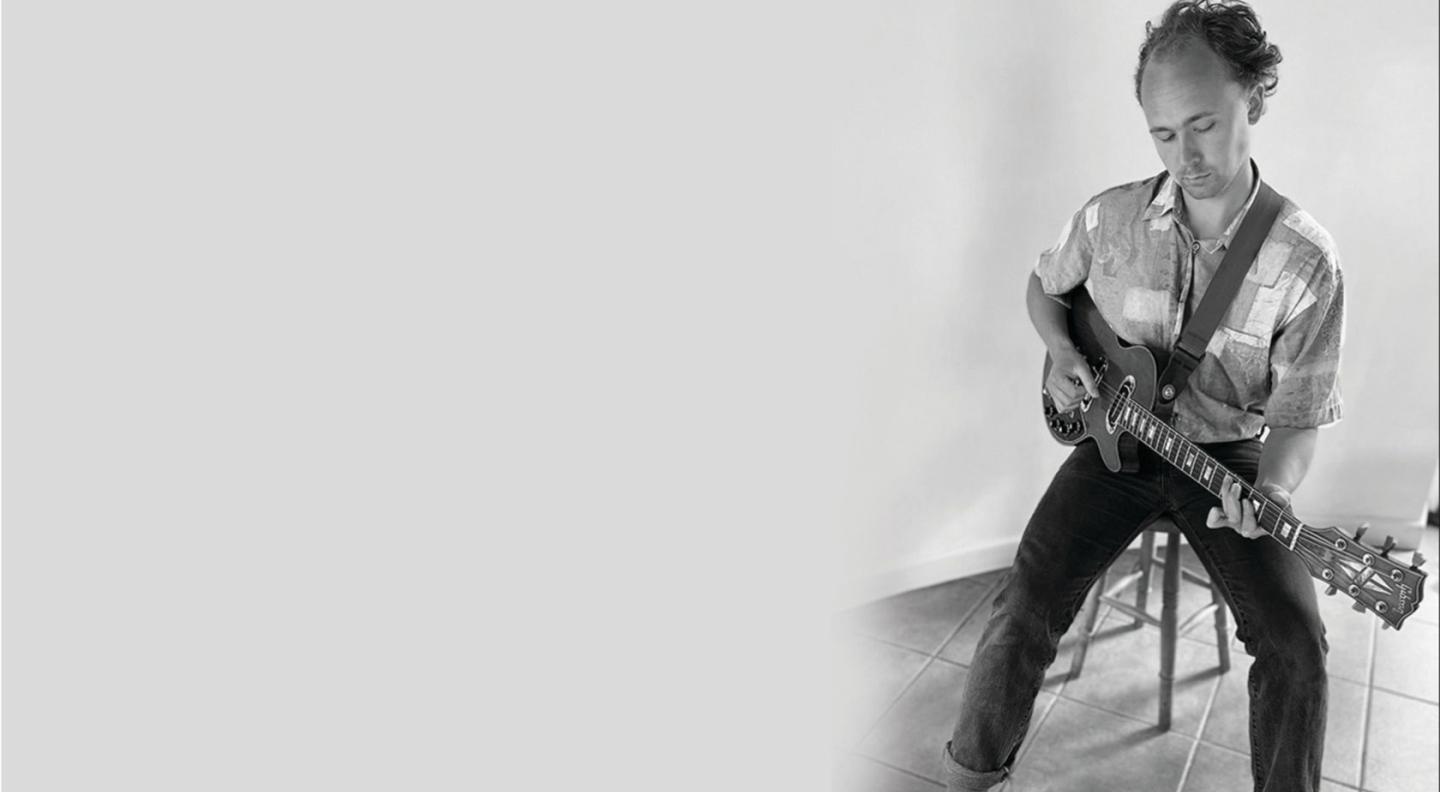 A photograph of Mark Lewis Heavenor playing the guitar in black and white