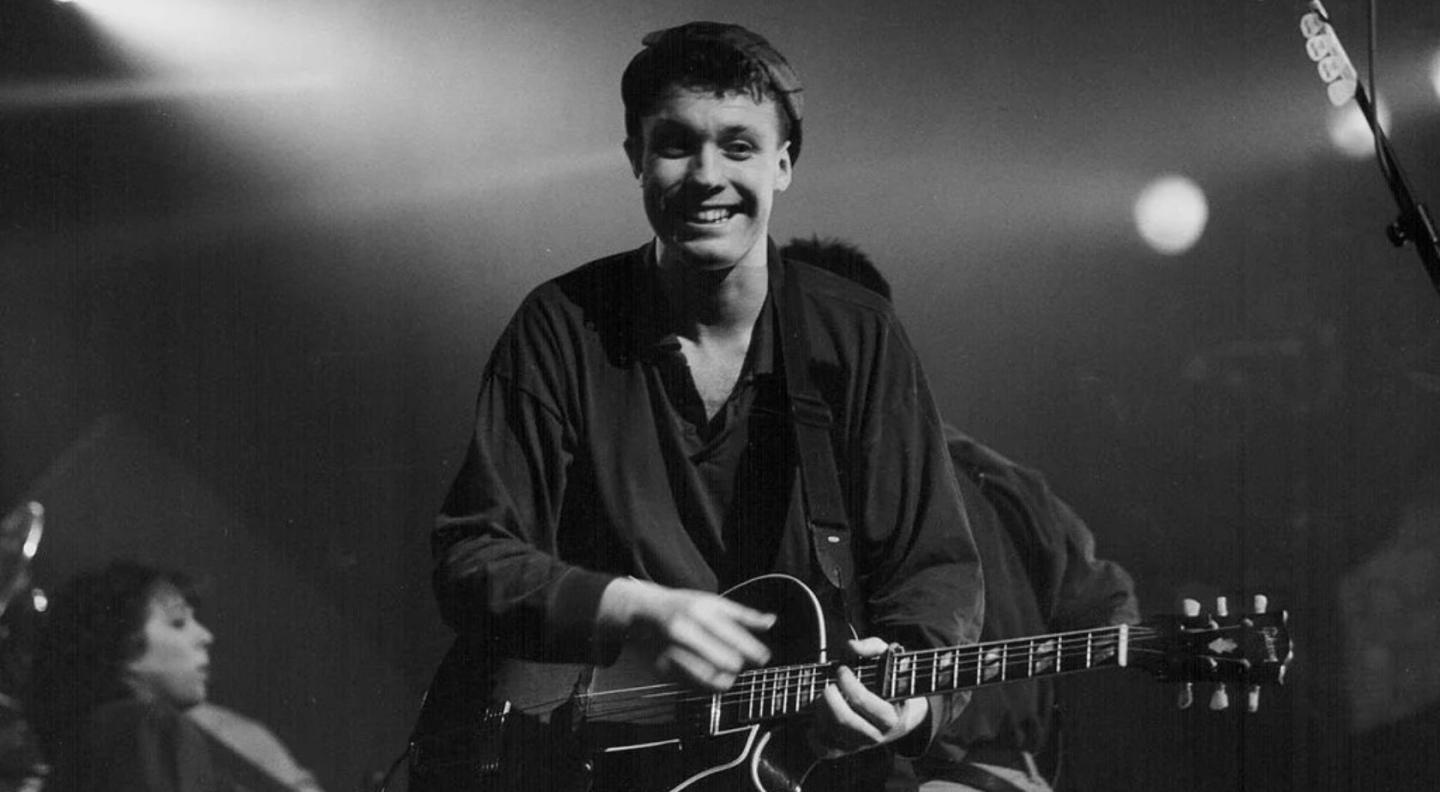 A young Martin Stephenson playing the guitar and smiling