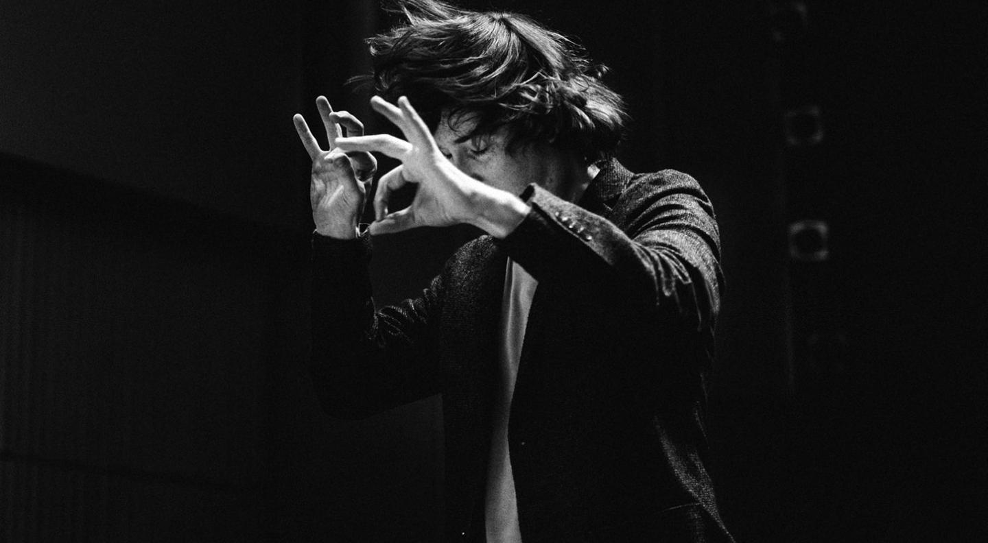 A black and white mid shot photograph of Maxim Emelyanychev conducting animatedly with his hair flying around