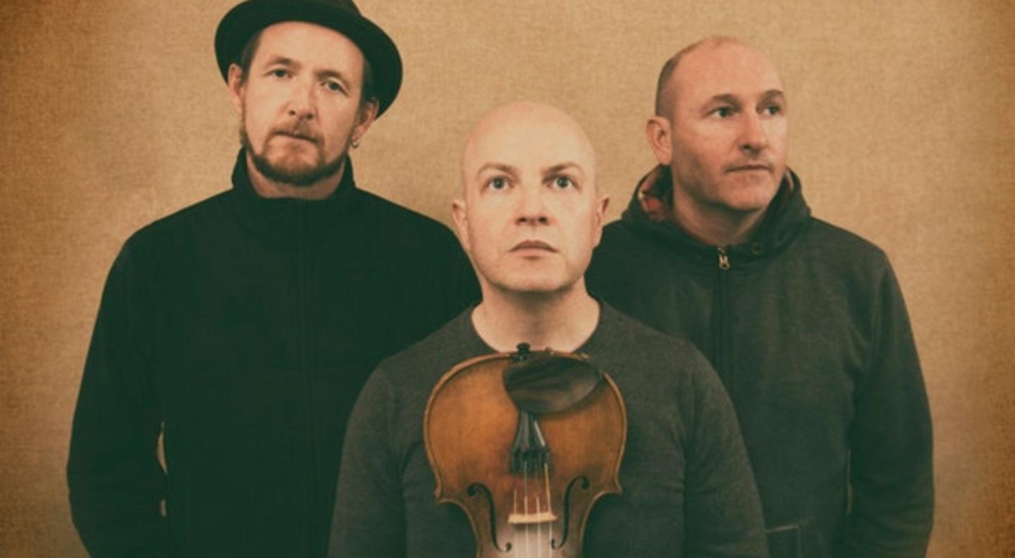 Michael McGoldrick, John McCusker (holding a fiddle) and John Doyle stand in a line