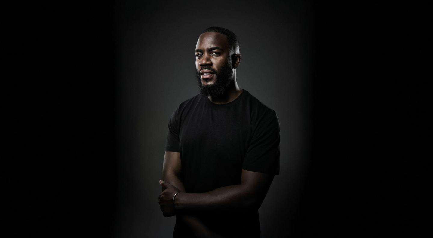 Comedian Mo Gilligan wearing a black t-shirt standing in front of a black background