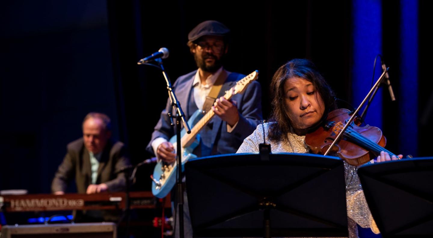 A close up shot of performers on The Queen's Hall stage playing a violin, a guitar and a Hammond organ