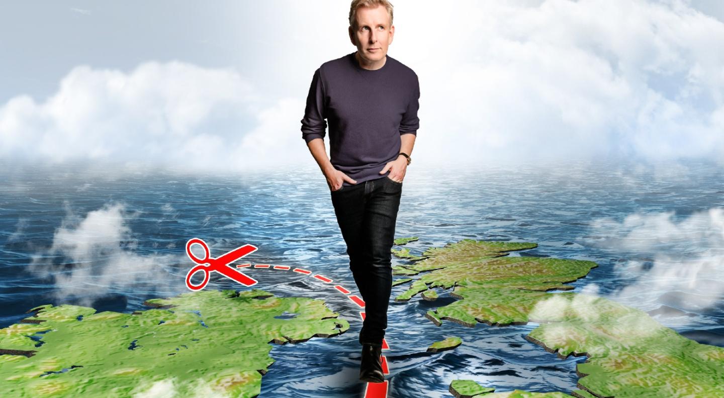 An illustration of Patrick Kielty walking along a red dotted line, with a pair of scissors at one end, which runs through the sea between the UK and the island of Ireland. Behind him the sky is grey and there are storm clouds