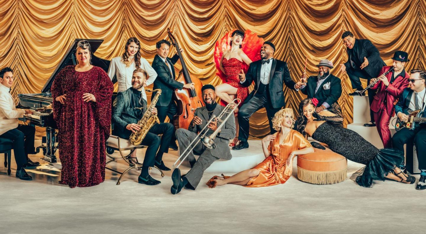 The artists in Post Modern Jukebox posing in front of a yellow curtain