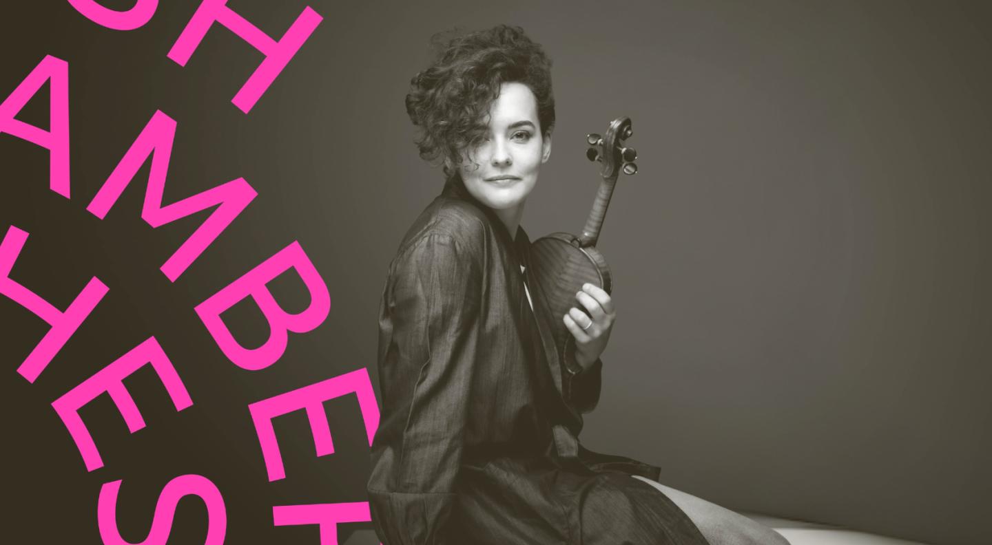 Alena Baeva, posing with her violin and looking at the camera