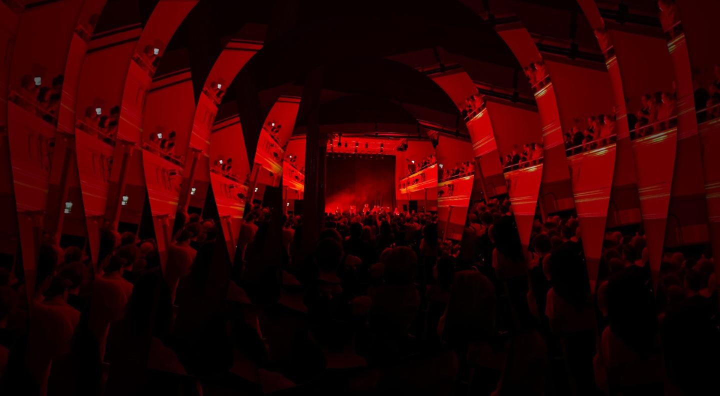A dark red image of the Queen's Hall venue in the middle of an event showing an audience enjoying a performance. The image has been tiled out to make a ripple effect of many images