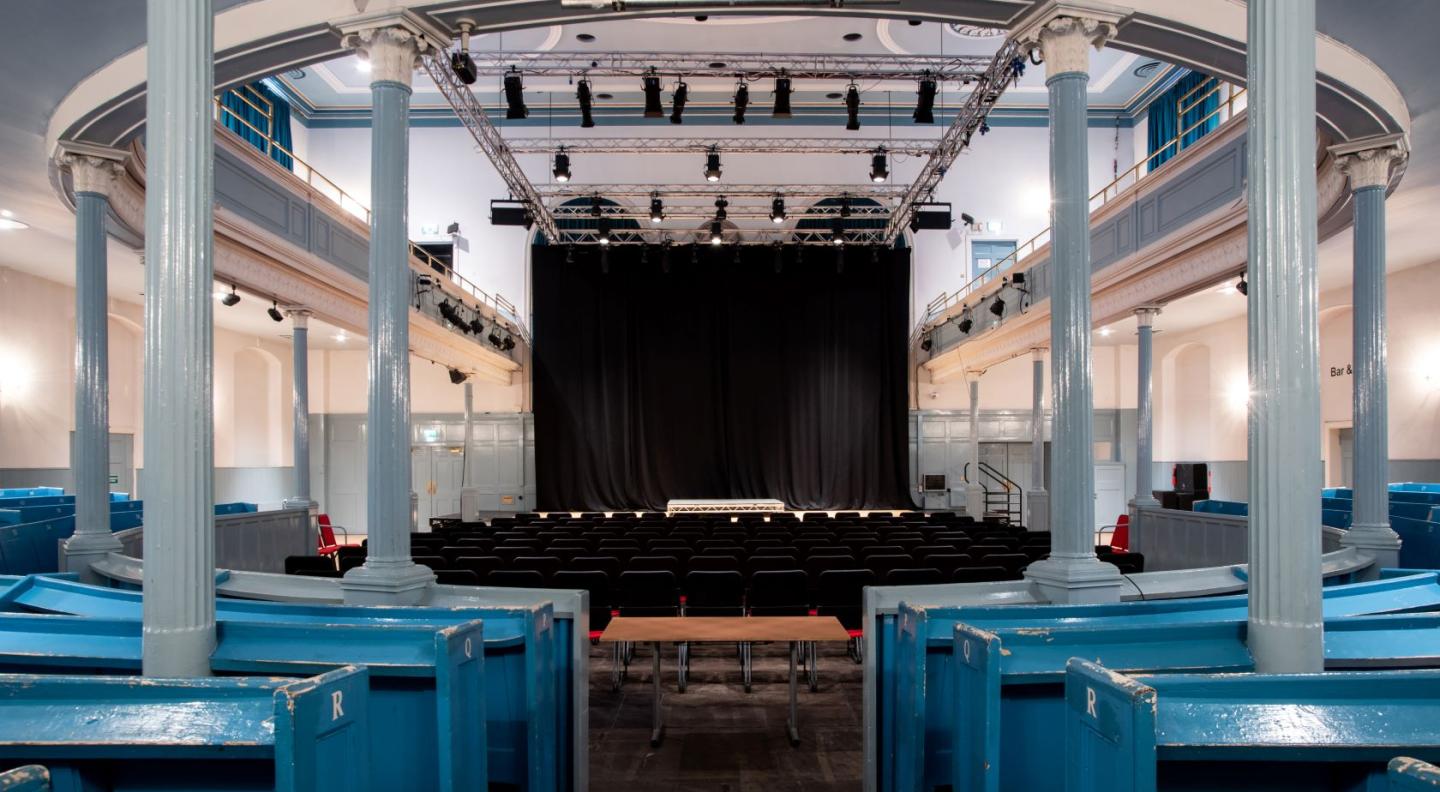 A view throught The Queen's Hall auditorium of a stage, seats and pillars