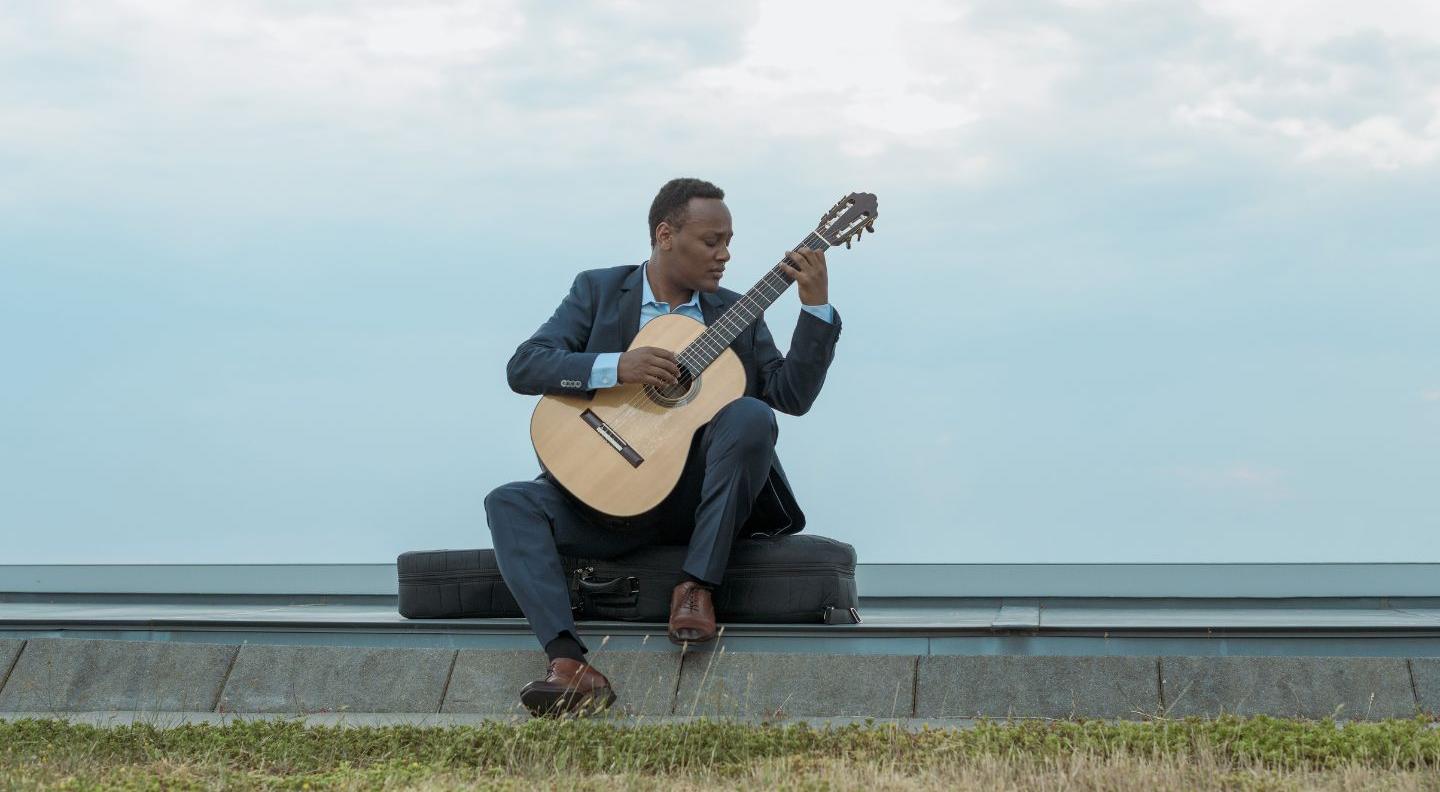 Rapahel sits on  a ledge playing guitar