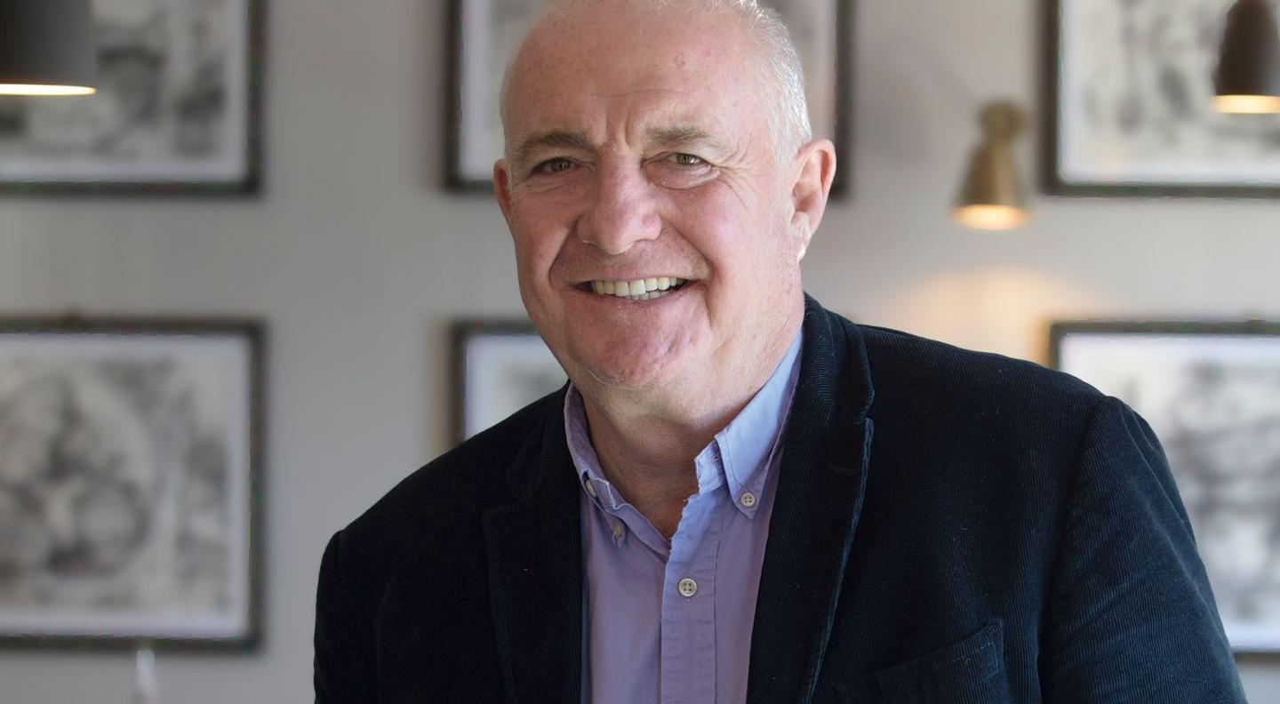 Rick Stein is a white man with white hair, wearing a dark suit and purple shirt
