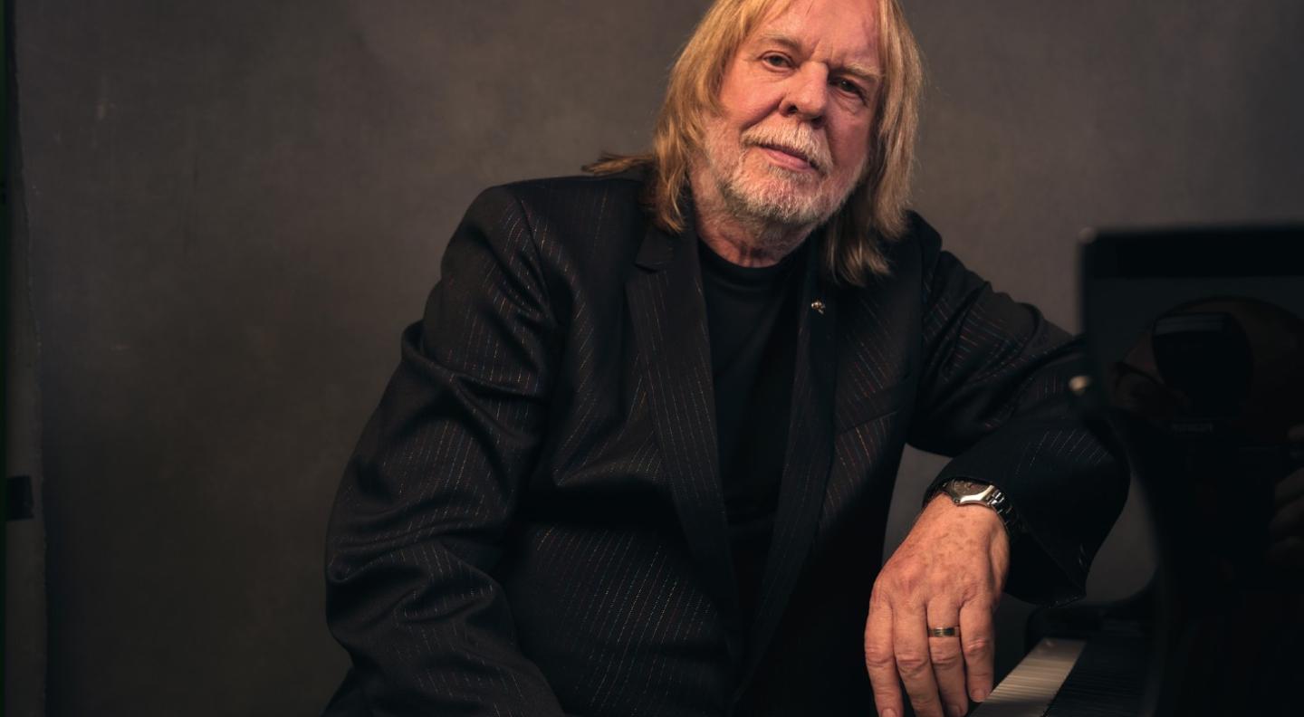 Rick Wakeman leans against a piano