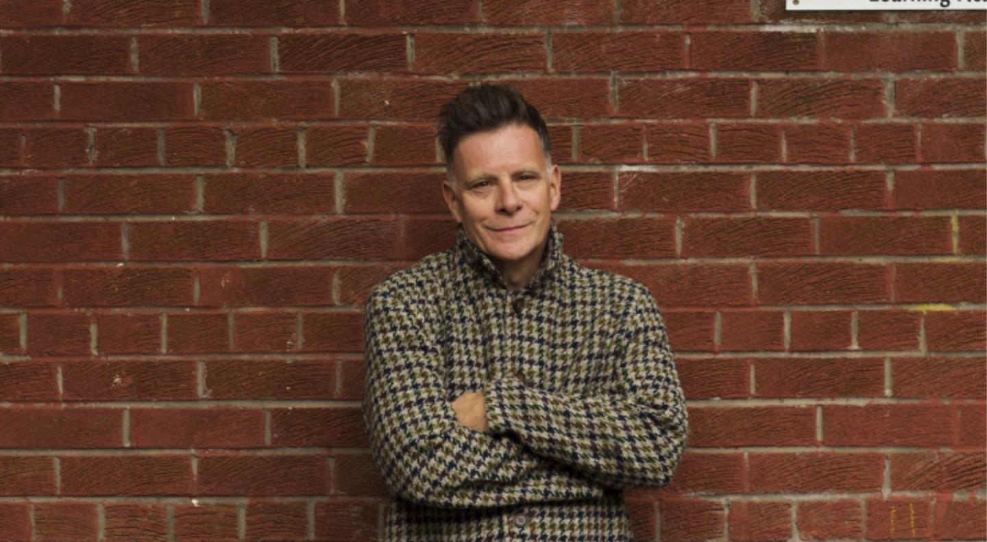 Ricky Ross stands, arms folded, in front of a red brick wall