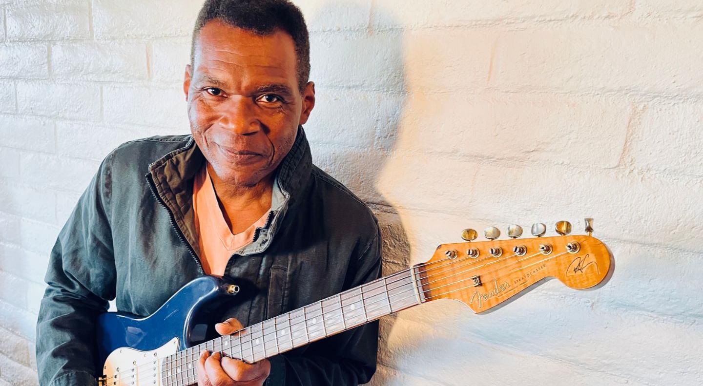 Robert Cray against a white background holding an electric guitar