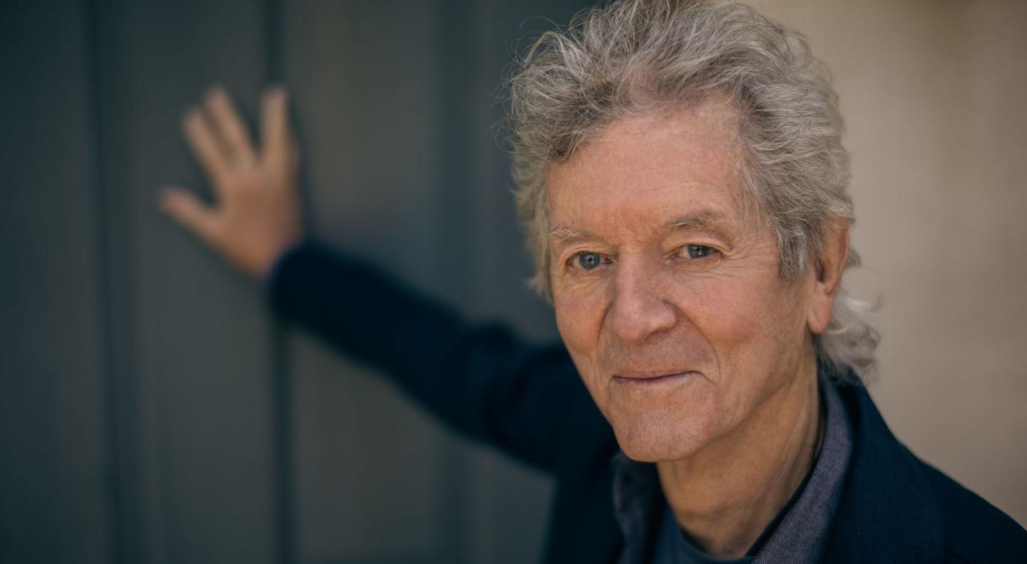 Rodney Crowell smiling at the camera leaning on a door
