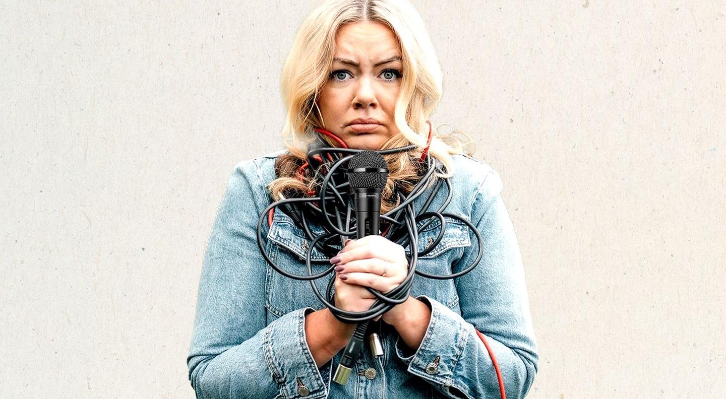 Serena Terry, a blonde white woman, stands against a cream background wrapped up in a microphone cable