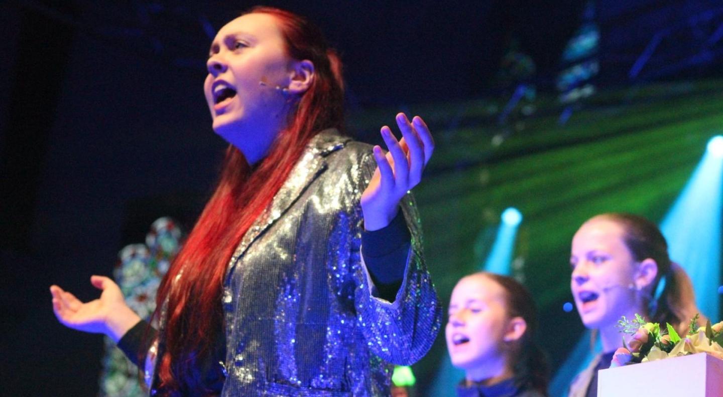 A young performer from SJM creative wearing a sparkly silver jacket, performing on stage