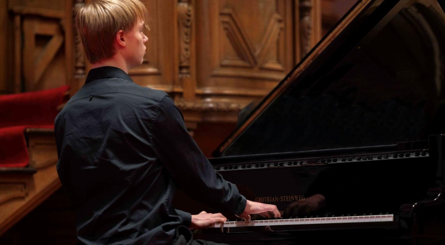 A pupil of St Mary's Music School, playing a grand piano with his back to the camera
