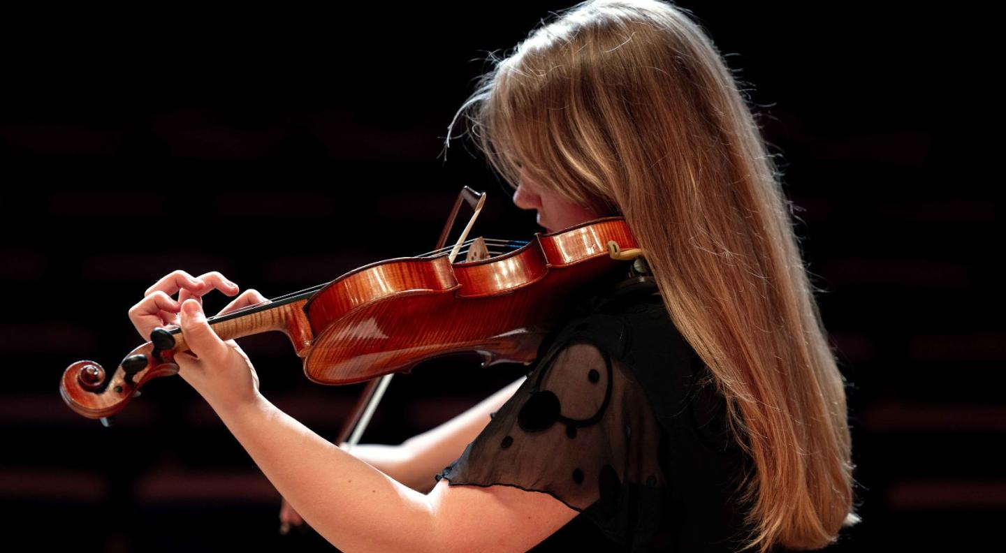 A female pupil of St Mary's Music School playing the violin, with her back to the camera