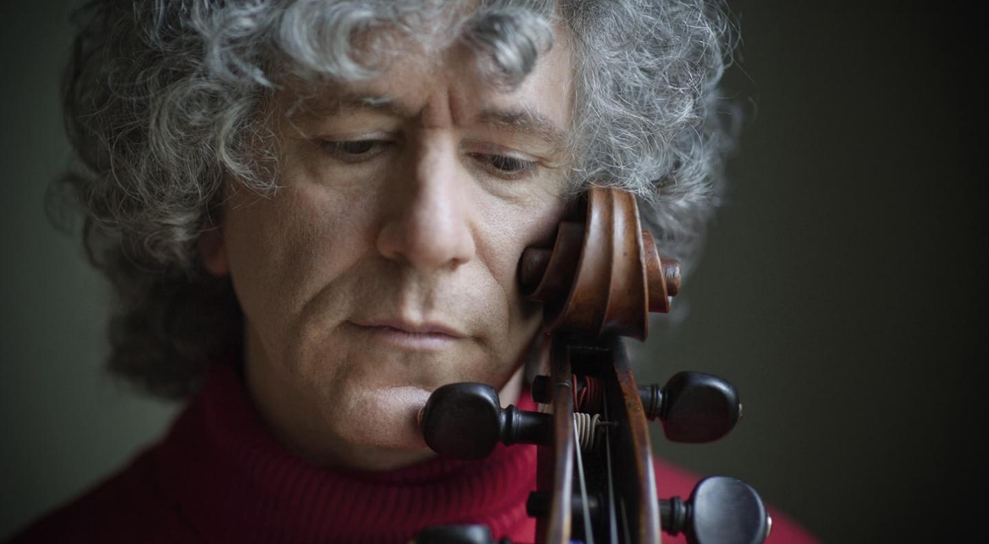 A close up full colour shot of Steven Isserlis with his eyes closed and the scroll at the top of the neck of the cello resting against his cheek