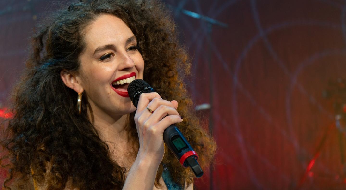 A woman with curly hair and red lipstick sings into a microphone