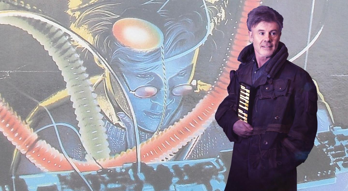 Thomas Dolby standing in front of the album cover artwork for his album 'The Golden Age of Wireless'