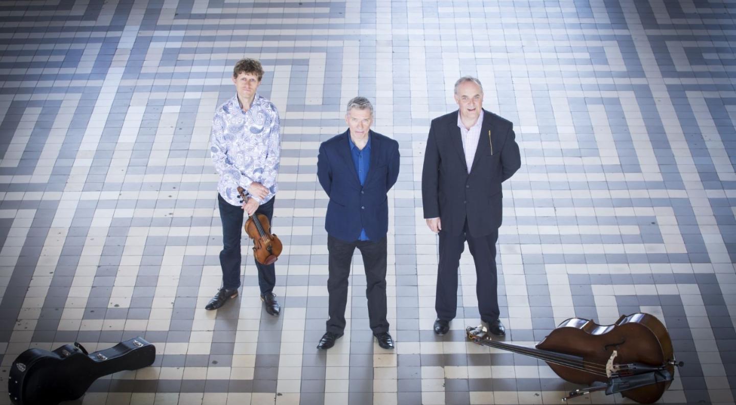 A photograph of the three members of the Tim Kliphuis Trio standing on a tiled floor.