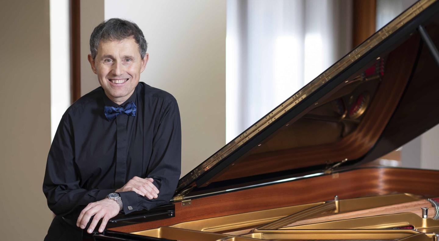 Stanev stands by a grand piano, smiling