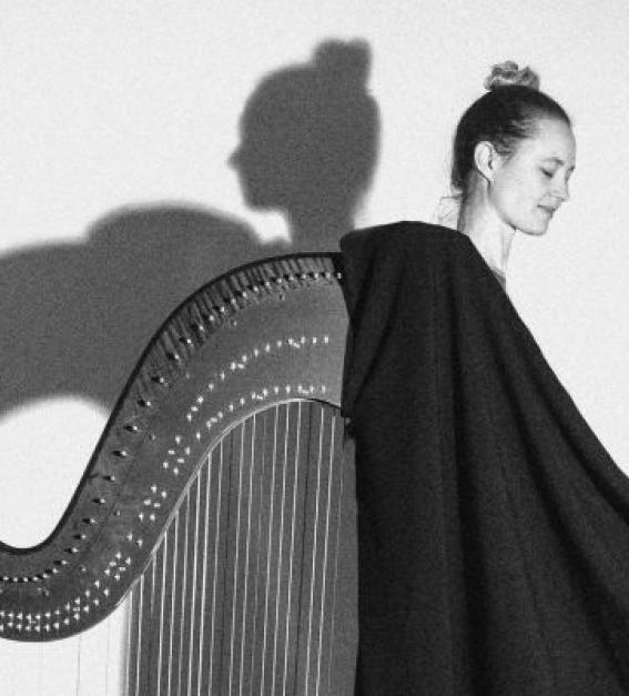 a black and white image of Esther Swift and her harp, casting a shadow on white wall