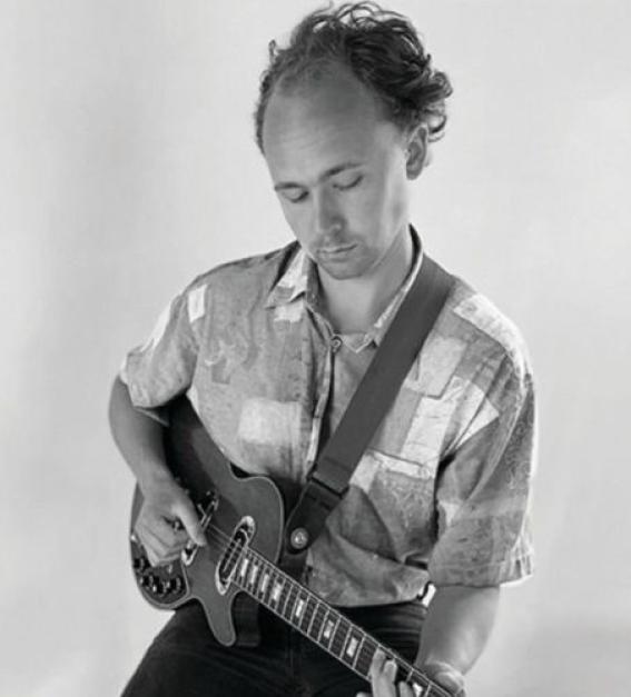 A photograph of Mark Lewis Heavenor playing the guitar in black and white