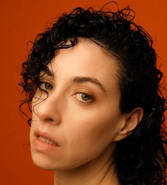 A woman with dark curly hair against a red backgroun