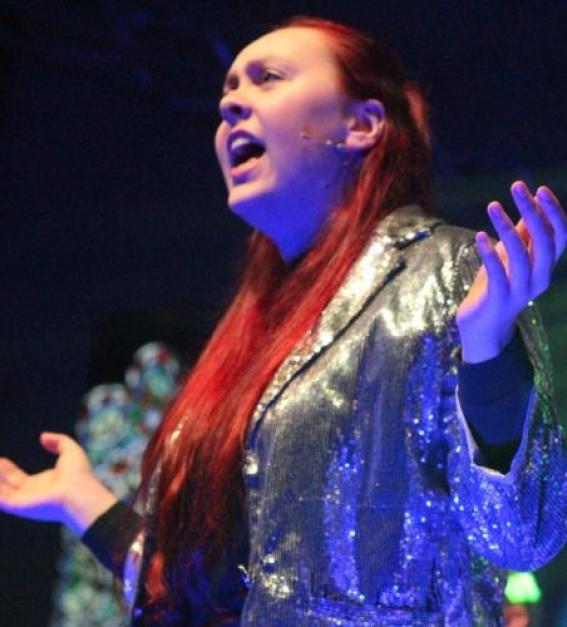 A young performer from SJM creative wearing a sparkly silver jacket, performing on stage