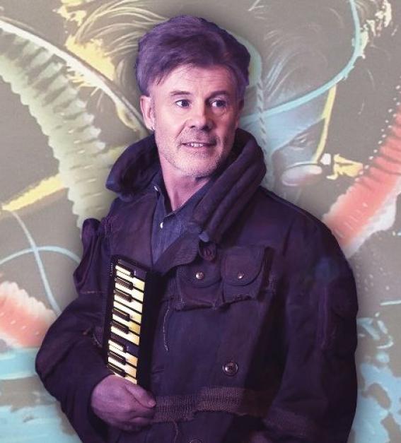 Thomas Dolby standing in front of the album cover artwork for his album 'The Golden Age of Wireless'